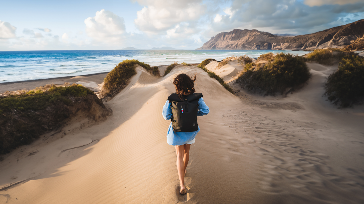 Eine Frau spaziert mit einem GOTBAG Rucksack an einem Strand